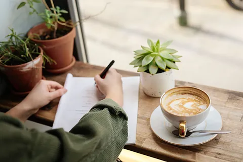 Person skriver på papirer med kaffekopp og planter på bordet